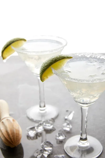 Selective focus of alcohol margarita cocktails with lime pieces and wooden squeezer on grey surface on white — Stock Photo