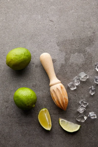 Flat lay with wooden squeezer, limes and ice cubes for cocktail on grey surface — Stock Photo