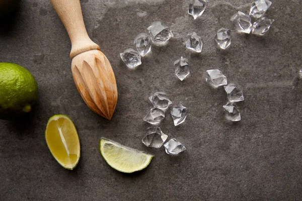 Flat lay with wooden squeezer, lime pieces and ice cubes for cocktail on grey surface — Stock Photo