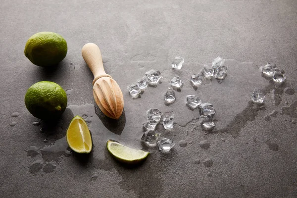 Close up view of wooden squeezer, limes and ice cubes for cocktail on grey surface — Stock Photo