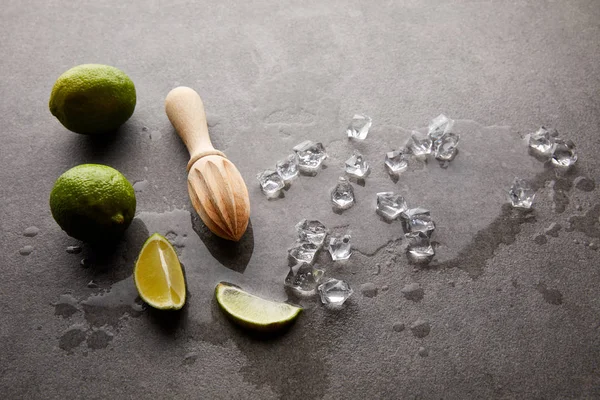 Vista de cerca de exprimidor de madera, limas y cubitos de hielo para cóctel en la superficie gris - foto de stock