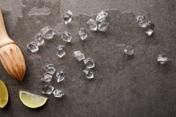 Draufsicht auf arrangierte Holzpresse, Limettenstücke und Eiswürfel für Cocktails auf grauer Oberfläche — Stockfoto