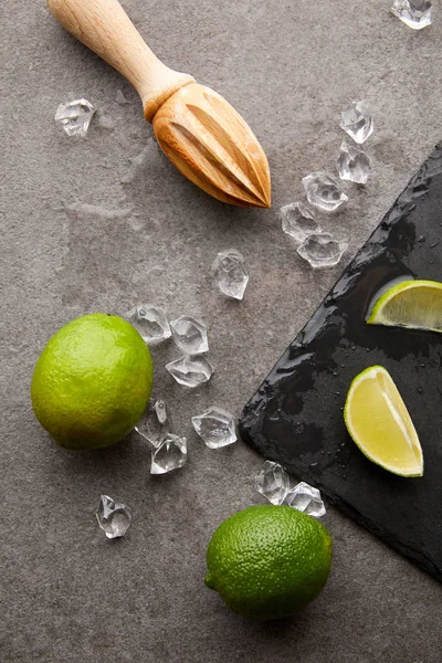 Flat lay with wooden squeezer, limes and ice cubes for cocktail on grey surface — Stock Photo