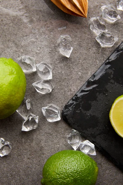 Tendido plano con exprimidor de madera, limas y cubitos de hielo para cóctel en superficie gris - foto de stock