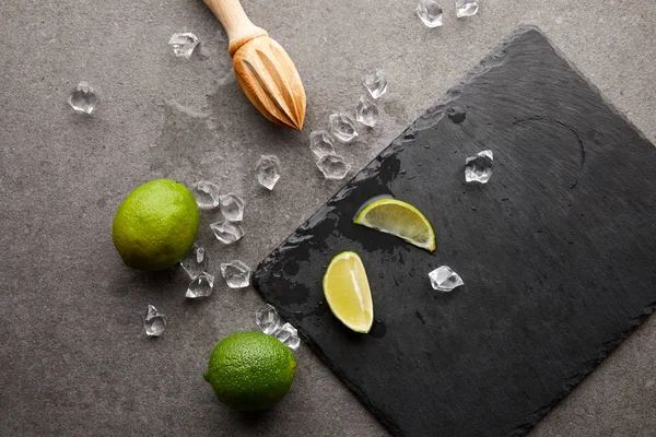 Tendido plano con exprimidor de madera, limas y cubitos de hielo para cóctel en superficie gris - foto de stock