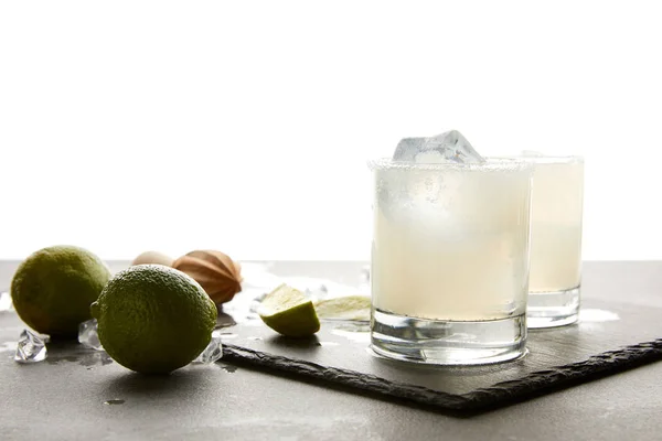 Close up view of refreshing sour alcohol cocktails with lime and ice on tabletop on white — Stock Photo