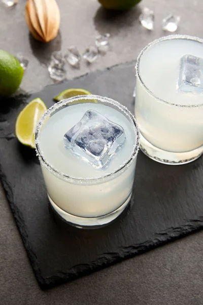 Vista de cerca del exprimidor de madera, refrescantes cócteles de alcohol agrio con lima y hielo en la mesa gris - foto de stock