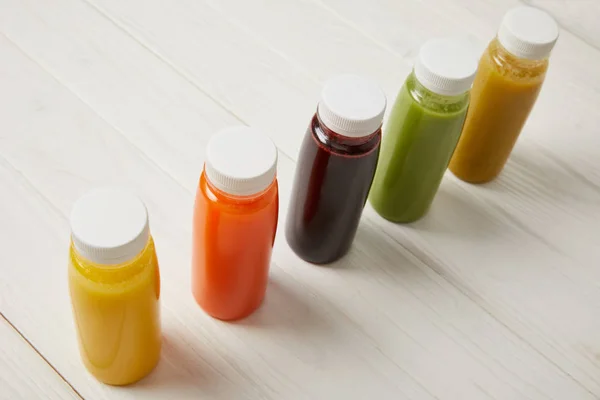 Disintossicazione frullati in bottiglie in piedi in fila su sfondo di legno bianco — Foto stock