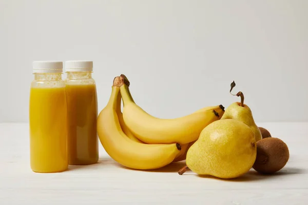 Bottles with yellow smoothies with bananas, pears and kiwis on white background — Stock Photo