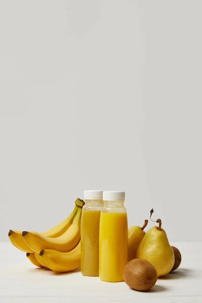 Flaschen mit gelben Smoothies mit Bananen, Birnen und Kiwis auf weißem Hintergrund — Stockfoto