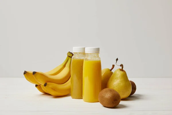 Batidos desintoxicantes amarillos en botellas con plátanos, peras y kiwis sobre fondo blanco - foto de stock
