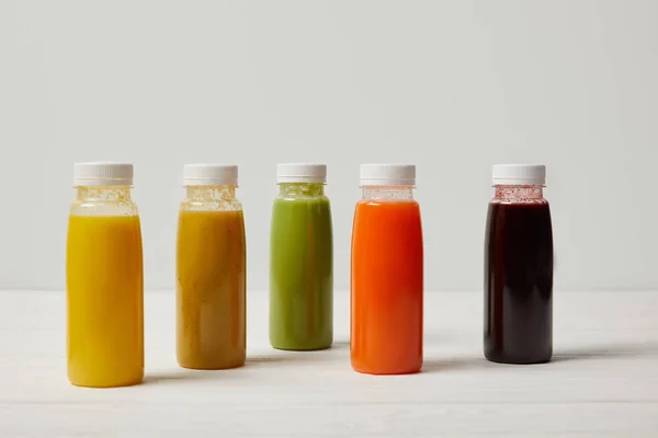 Smoothies de désintoxication colorés en bouteilles sur une surface en bois blanc — Photo de stock