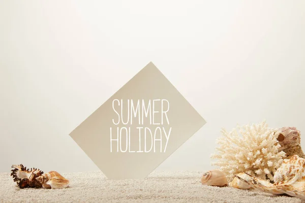 Vista de perto de coral, conchas e cartão com letras de férias de verão na areia sobre fundo cinza — Fotografia de Stock