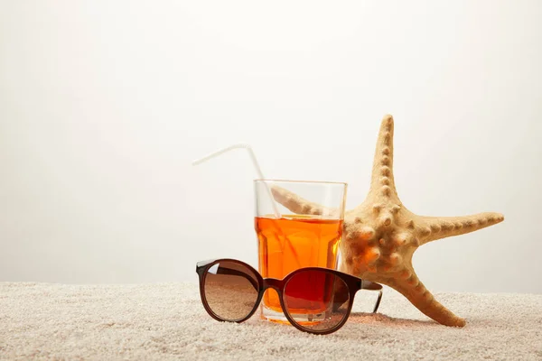 Nahaufnahme Sonnenbrille, Cocktail mit Stroh und Seestern auf Sand vor grauem Hintergrund — Stockfoto