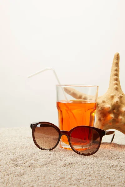 Vue rapprochée des lunettes de soleil, cocktail avec paille et étoile de mer sur sable sur fond gris — Photo de stock