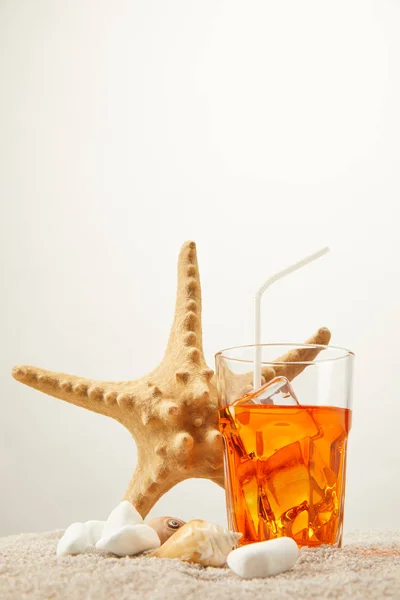 Nahaufnahme des Seesterns, erfrischender Cocktail mit Stroh und Muscheln auf Sand vor grauem Hintergrund — Stockfoto