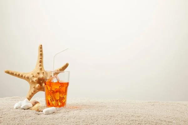 Close up view of sea star, refreshing cocktail with straw and seashells on sand on grey background — Stock Photo