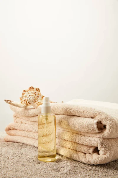 Close up view of arranged pile of towels, seashell and tanning oil on sand on grey backdrop — Stock Photo