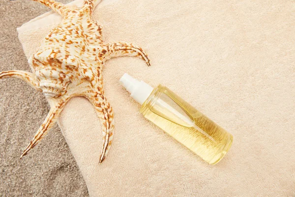 Vista dall'alto di mucchio organizzato di asciugamani, conchiglia e olio abbronzante sulla sabbia — Foto stock