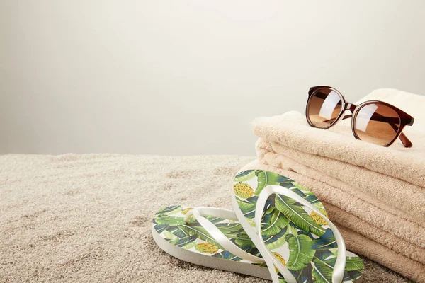 Vista de cerca de la pila de toallas, gafas de sol y chanclas de verano sobre arena sobre fondo gris - foto de stock