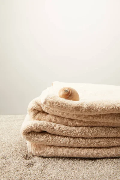 Vue rapprochée de la pile de serviettes avec coquillage sur sable sur fond gris — Photo de stock