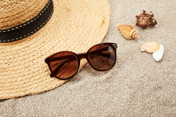 Крупним планом вид на солом'яний капелюх, черепашки і сонцезахисні окуляри на піску — стокове фото
