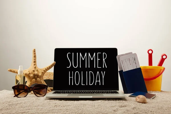 Nahaufnahme von Laptop mit Sommerurlaubsaufdruck, Seestern, Sonnenbrille, Reisepässen mit Tickets und Spielzeugeimer auf Sand auf grauem Hintergrund — Stockfoto