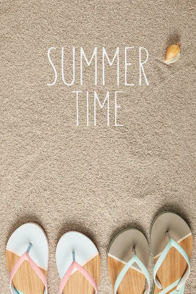 Flat lay with summertime lettering, flip flops and seashell on sand — Stock Photo