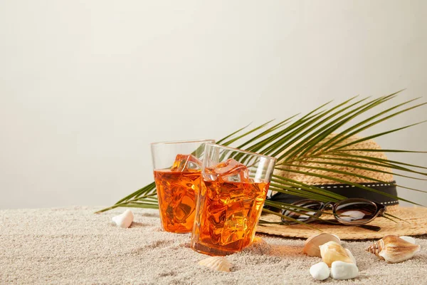 Nahaufnahme von Strohhut, Cocktails, Muscheln, Sonnenbrille und Palmblatt auf Sand vor grauem Hintergrund — Stockfoto