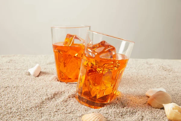 Nahaufnahme von Gläsern mit erfrischenden Cocktails auf Sand mit Muscheln auf grauem Bakgorund — Stockfoto
