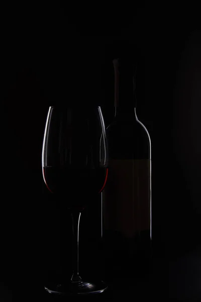 Primer plano de botella y vidrio con vino tinto aislado sobre fondo negro - foto de stock