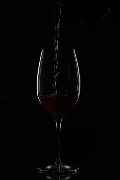 Nahaufnahme von Rotwein, der aus einer Flasche auf schwarzem Hintergrund in ein Glas gegossen wird — Stockfoto