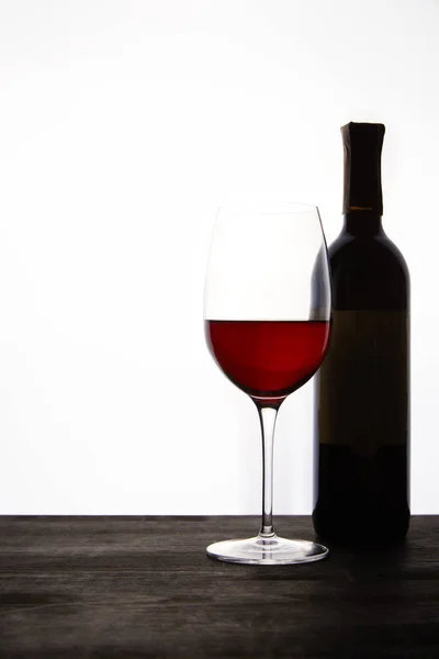 Vista de cerca de la botella y el vaso con vino tinto en la mesa de madera oscura - foto de stock