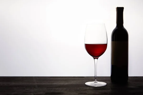 Botella y vaso con vino tinto sobre mesa de madera oscura - foto de stock