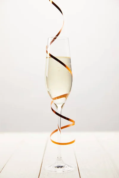 Closeup view of champagne glass wrapped by serpentine on white wooden table, holiday concept — Stock Photo