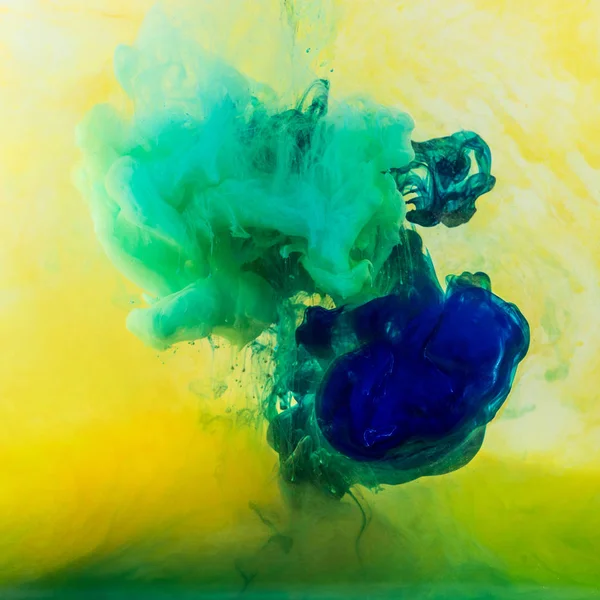 Turbinii astratti di vernice verde e blu che scorre in acqua gialla — Foto stock