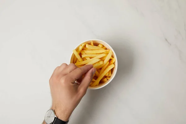 Ansicht von oben: Mann nimmt Pommes aus Schüssel auf weiß — Stockfoto