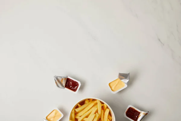 Top view of french fries in bowl surrounded with containers of sauces on white — Stock Photo