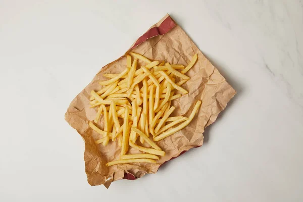 Vue de dessus de délicieuses frites renversées sur du papier froissé sur du blanc — Photo de stock