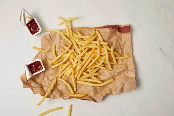 Вид зверху картоплі фрі на збитому папері з контейнерами кетчупу на білому — стокове фото