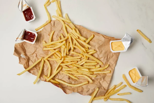 Top view of french fries on crumpled paper with containers of sauces on white — Stock Photo