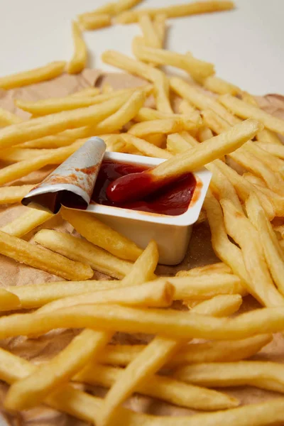 French fries on crumpled paper with container of ketchup — Stock Photo