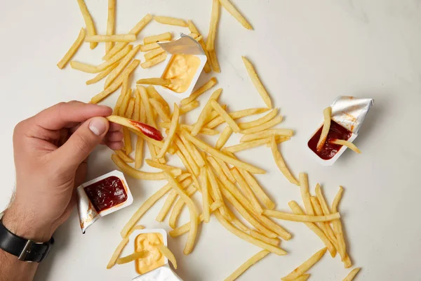 Recortado disparo de hombre tomando papas fritas de la superficie blanca - foto de stock