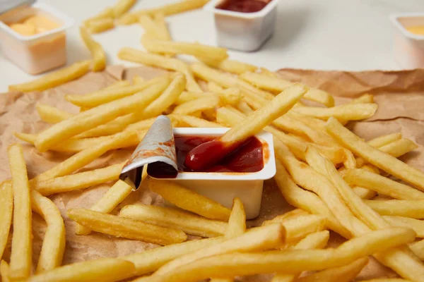 Close-up shot of french fries on crumpled paper with containers of sauces — Stock Photo