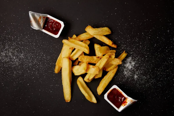 Vista superior de batatas fritas com recipientes de ketchup em preto — Fotografia de Stock