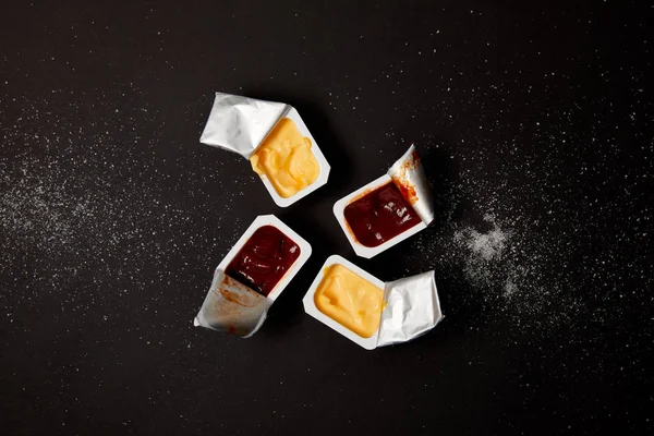 Top view of plastic containers with sauces on black surface spilled with salt — Stock Photo