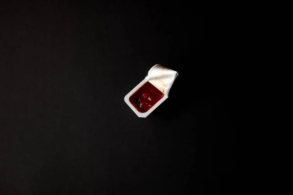 Top view of plastic container with ketchup isolated on black — Stock Photo