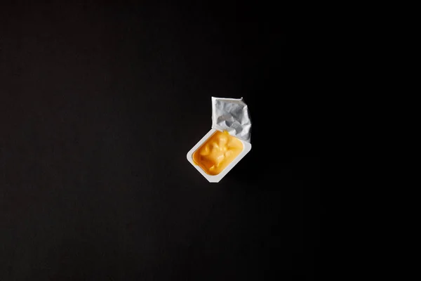 Вид сверху пластикового контейнера с сырным соусом, изолированным на черном — стоковое фото