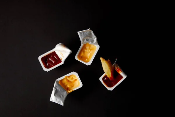 Top view of plastic containers with sauces and poured french fry isolated on black — Stock Photo