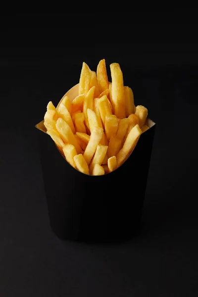 Close-up shot of black box of tasty french fries isolated on black isolated on black — Stock Photo
